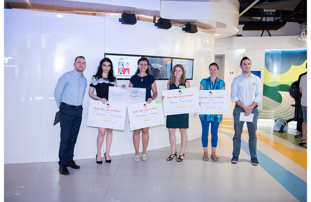 Group of six people standing indoors holding large scholarship checks during an award event.