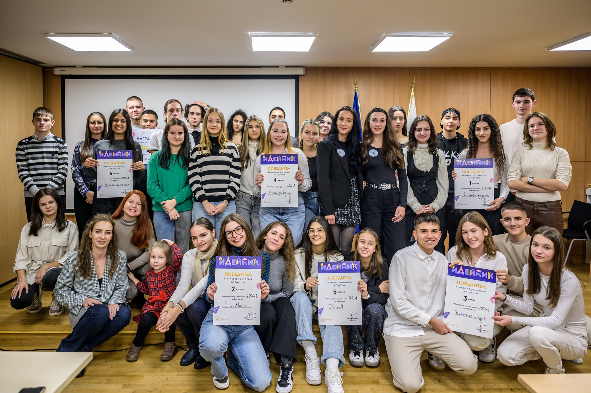 Large group of young people posing indoors, some holding certificates and smiling. Winners from Ideinik 2024
